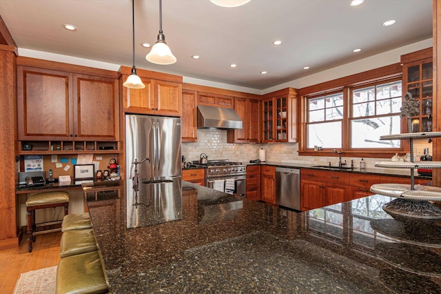 kitchen with sink, appliances with stainless steel finishes, decorative light fixtures, dark stone counters, and wall chimney exhaust hood