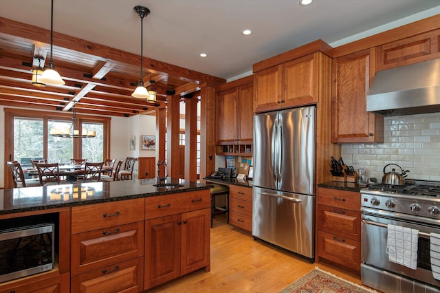 kitchen featuring wall chimney exhaust hood, sink, decorative light fixtures, dark stone countertops, and stainless steel appliances