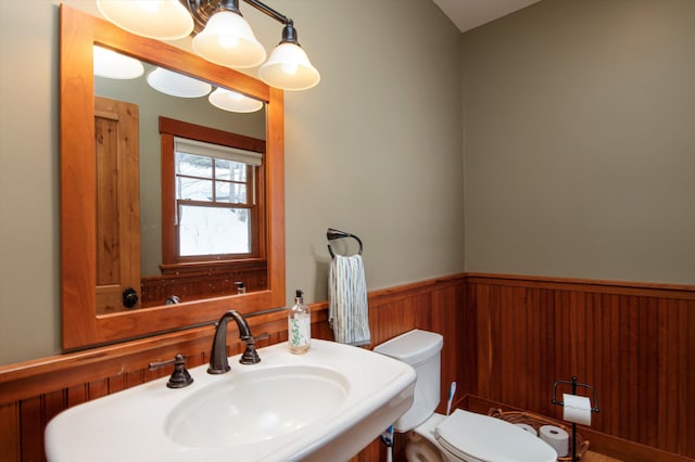 bathroom featuring toilet, sink, and wood walls