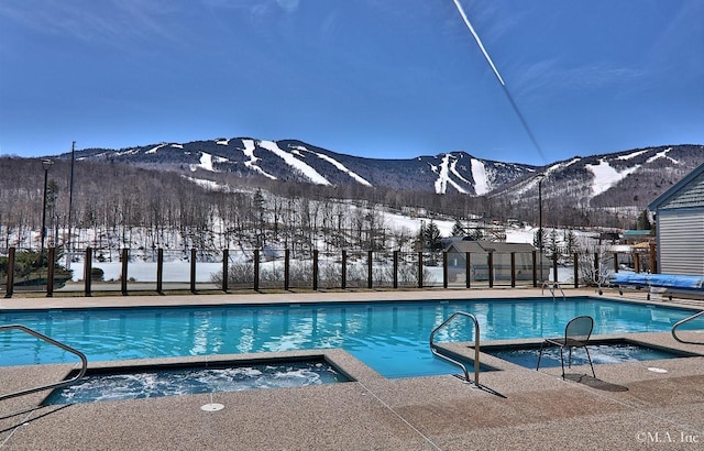 snow covered pool with a hot tub and a mountain view