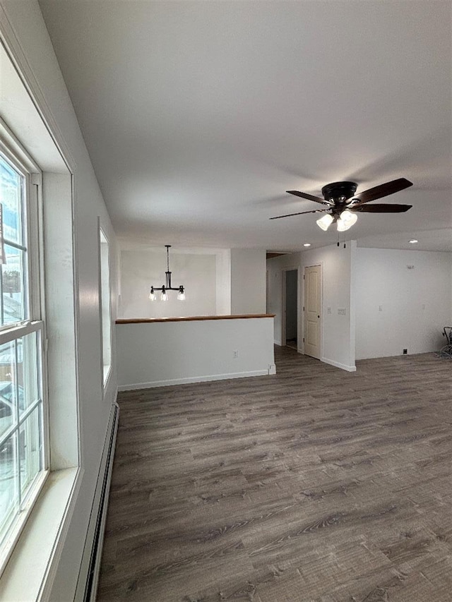 unfurnished living room with dark hardwood / wood-style floors, ceiling fan with notable chandelier, and a baseboard heating unit