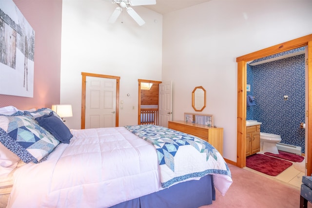 bedroom with ceiling fan, baseboard heating, ensuite bathroom, a high ceiling, and light carpet