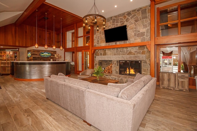 living room with a stone fireplace, high vaulted ceiling, bar, a notable chandelier, and light hardwood / wood-style flooring