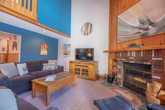 living room featuring carpet flooring, wooden walls, a fireplace, and a towering ceiling