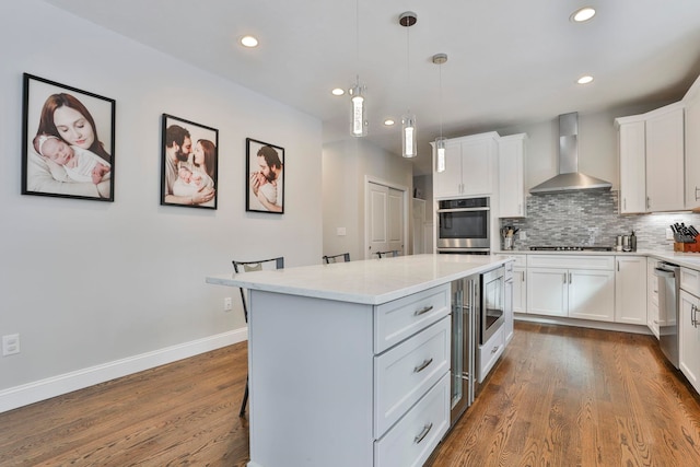 kitchen with white cabinetry, hanging light fixtures, a kitchen island, stainless steel appliances, and wall chimney range hood