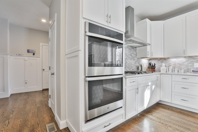 kitchen with dark wood-type flooring, white cabinets, appliances with stainless steel finishes, and wall chimney range hood