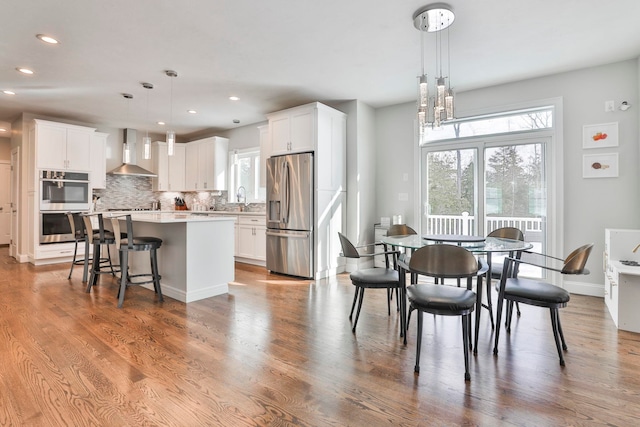 kitchen featuring wall chimney exhaust hood, appliances with stainless steel finishes, decorative light fixtures, and white cabinets