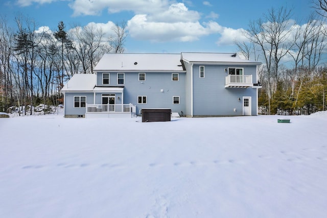 snow covered rear of property with a balcony and covered porch