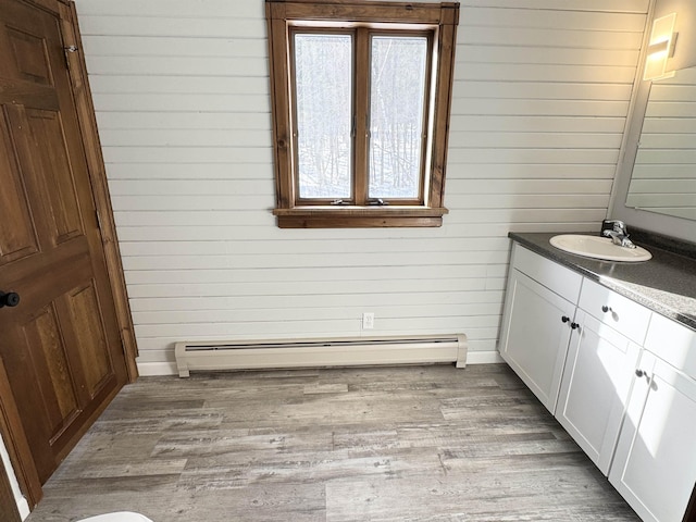 bathroom featuring wood walls, wood-type flooring, vanity, and a baseboard heating unit