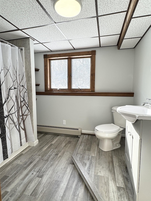 bathroom with vanity, wood-type flooring, a drop ceiling, a baseboard radiator, and toilet