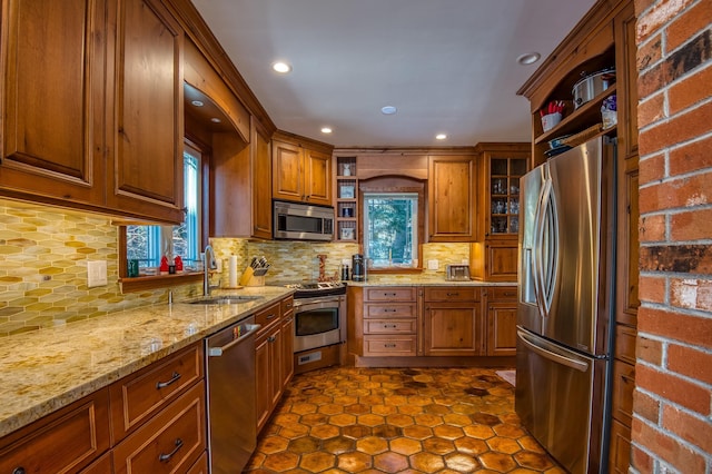 kitchen with sink, dark tile patterned floors, stainless steel appliances, tasteful backsplash, and light stone countertops