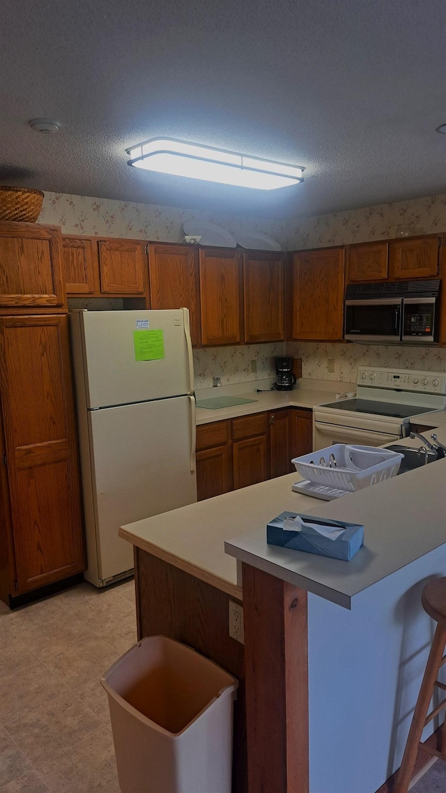 kitchen featuring white appliances, a breakfast bar area, and a textured ceiling