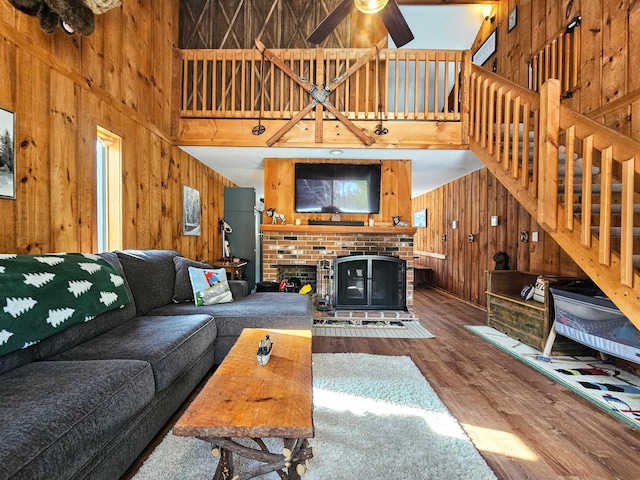 living room with a fireplace, hardwood / wood-style flooring, wooden walls, and a towering ceiling