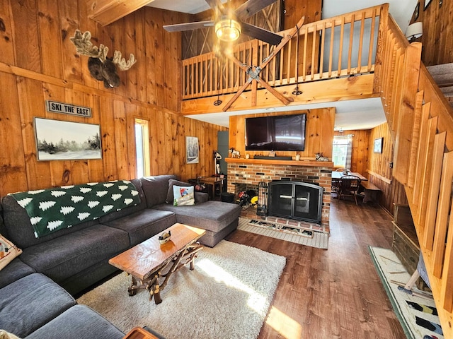 living room featuring wood walls, a brick fireplace, ceiling fan, dark hardwood / wood-style flooring, and a towering ceiling