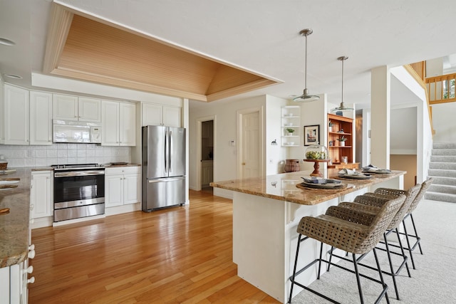 kitchen with stone countertops, hanging light fixtures, a raised ceiling, stainless steel appliances, and white cabinets