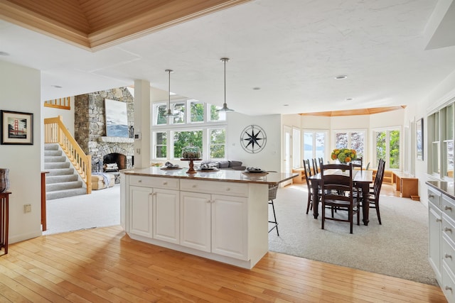 kitchen with a stone fireplace, a center island, light wood-type flooring, pendant lighting, and white cabinets