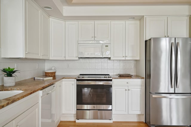 kitchen with tasteful backsplash, white cabinets, stainless steel appliances, light stone countertops, and light wood-type flooring