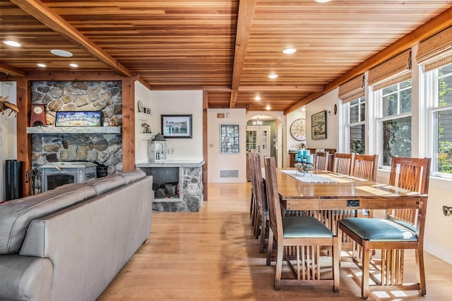 dining space with beamed ceiling, light wood-type flooring, wood ceiling, and a fireplace