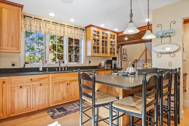 kitchen with hanging light fixtures, sink, a kitchen breakfast bar, and light wood-type flooring