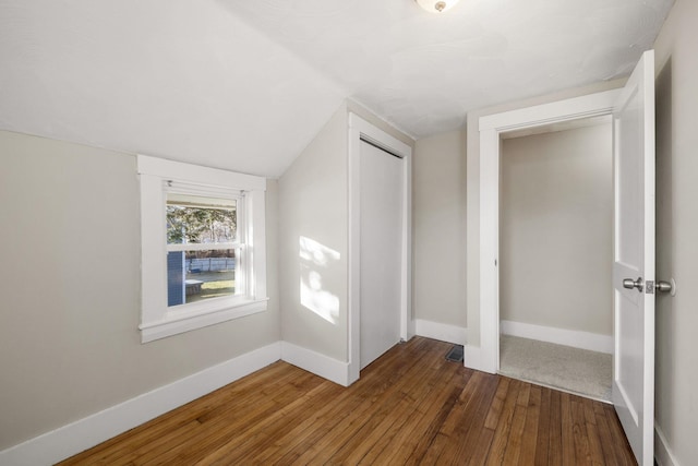 unfurnished bedroom with dark hardwood / wood-style floors, vaulted ceiling, and a closet