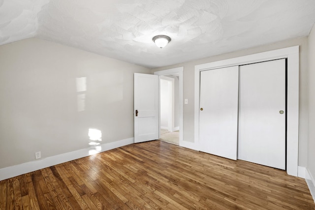 unfurnished bedroom featuring lofted ceiling, wood-type flooring, a closet, and a textured ceiling