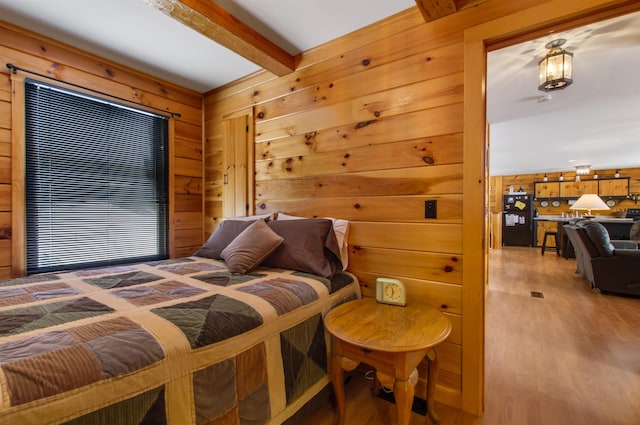 bedroom with black fridge, hardwood / wood-style floors, beam ceiling, and wood walls