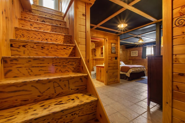 stairs featuring coffered ceiling, beam ceiling, and wood walls