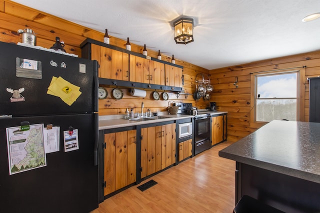 kitchen featuring sink, wood walls, light hardwood / wood-style floors, and black appliances