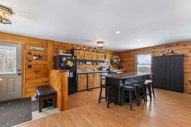 kitchen featuring sink, a breakfast bar area, wood walls, black fridge, and light hardwood / wood-style flooring