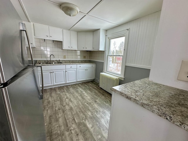 kitchen with white cabinetry, light hardwood / wood-style flooring, radiator heating unit, stainless steel fridge, and decorative backsplash