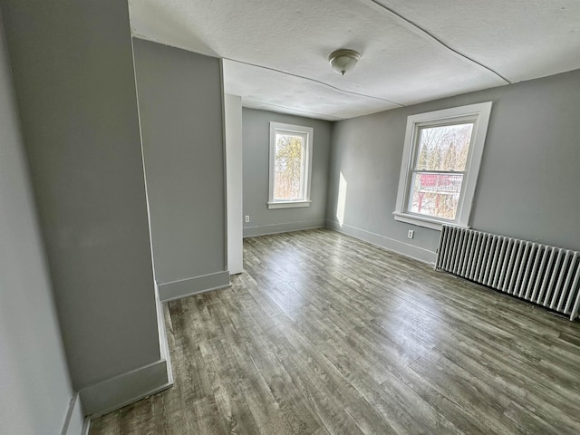 empty room with hardwood / wood-style floors, radiator heating unit, and a textured ceiling