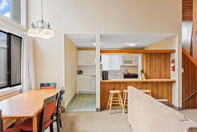 kitchen with black stove, decorative light fixtures, kitchen peninsula, light colored carpet, and white cabinets