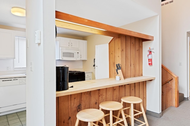 kitchen with white appliances, dark tile patterned floors, a kitchen breakfast bar, white cabinets, and kitchen peninsula