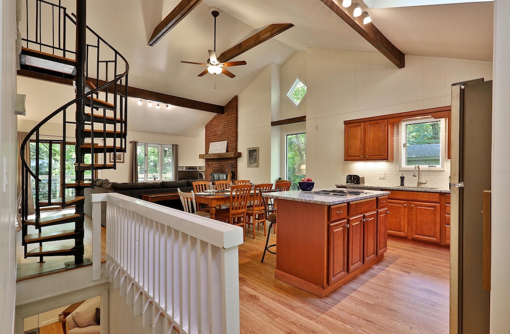 kitchen with beam ceiling, stainless steel appliances, a center island, light hardwood / wood-style floors, and a brick fireplace