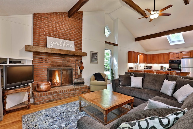 living room featuring a skylight, beamed ceiling, sink, a brick fireplace, and light hardwood / wood-style flooring