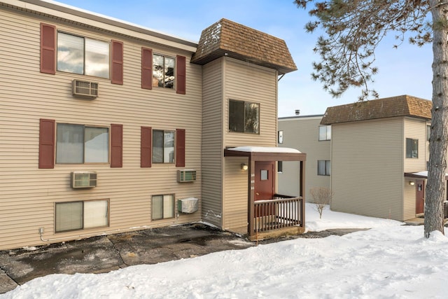 snow covered rear of property with a wall unit AC