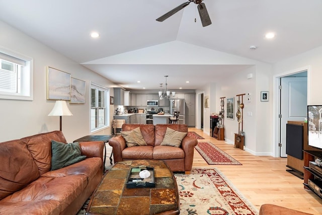 living room with lofted ceiling, ceiling fan with notable chandelier, and light hardwood / wood-style floors