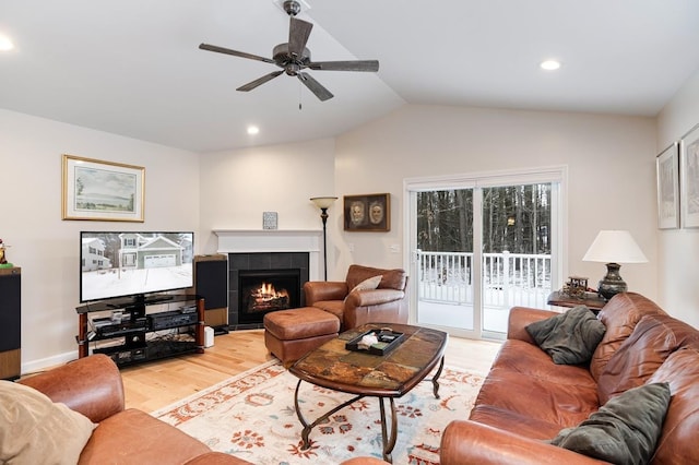 living room with a tile fireplace, vaulted ceiling, ceiling fan, and light wood-type flooring