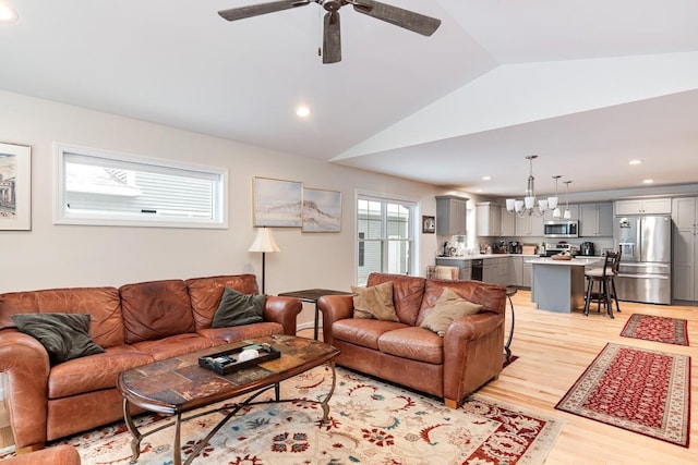 living room with vaulted ceiling, ceiling fan with notable chandelier, and light hardwood / wood-style flooring