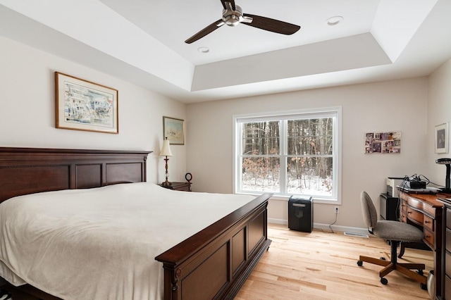 bedroom with ceiling fan, a tray ceiling, and light hardwood / wood-style floors