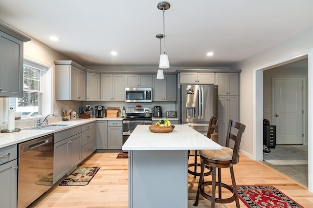 kitchen with pendant lighting, gray cabinets, light hardwood / wood-style flooring, appliances with stainless steel finishes, and a kitchen island