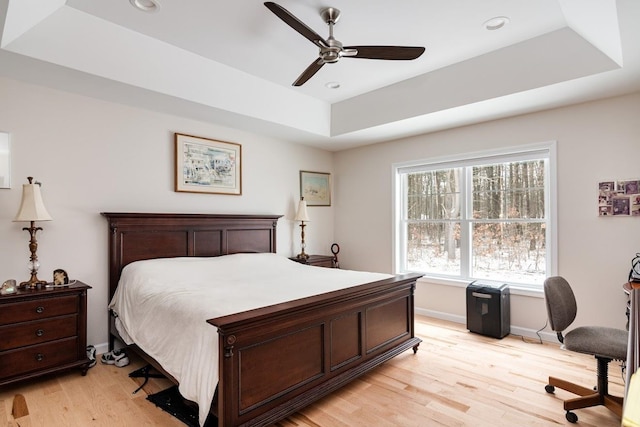 bedroom featuring a raised ceiling, ceiling fan, and light wood-type flooring