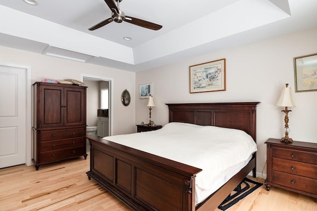 bedroom featuring a raised ceiling, ceiling fan, connected bathroom, and light wood-type flooring