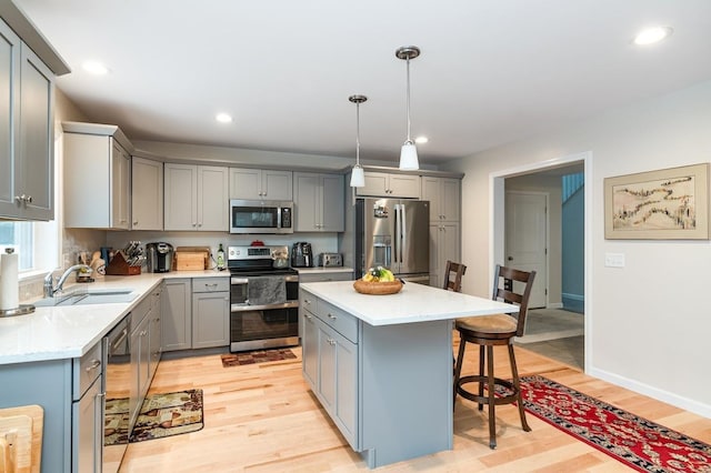 kitchen with a kitchen island, appliances with stainless steel finishes, sink, hanging light fixtures, and light wood-type flooring