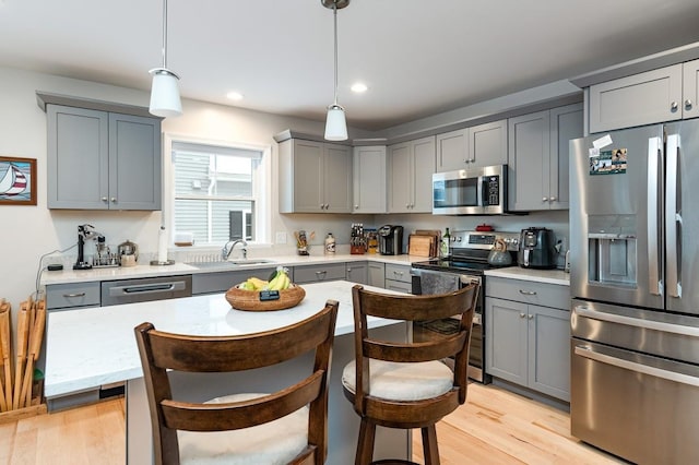 kitchen with pendant lighting, appliances with stainless steel finishes, light wood-type flooring, and gray cabinetry