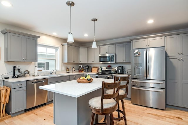 kitchen with gray cabinets, stainless steel appliances, light hardwood / wood-style floors, a kitchen island, and decorative light fixtures