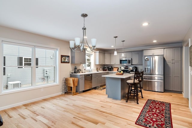 kitchen featuring gray cabinets, a kitchen island, appliances with stainless steel finishes, a breakfast bar, and decorative light fixtures