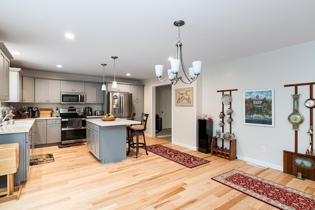 kitchen with appliances with stainless steel finishes, gray cabinetry, a kitchen island, a kitchen bar, and decorative light fixtures