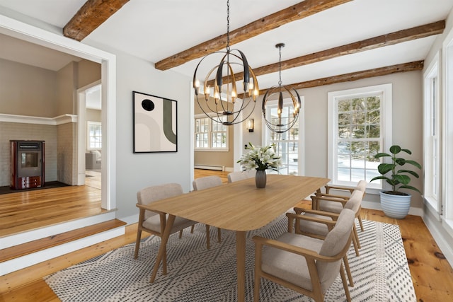 dining space featuring a fireplace, light wood-type flooring, a chandelier, a baseboard heating unit, and beam ceiling