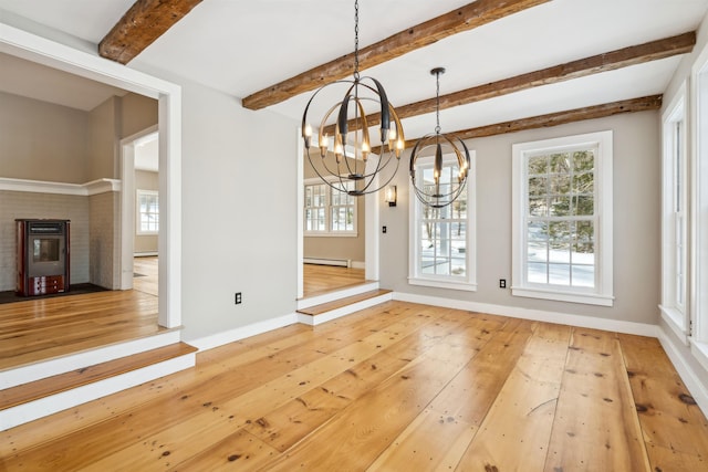 unfurnished dining area featuring a brick fireplace, baseboard heating, a notable chandelier, beam ceiling, and hardwood / wood-style floors